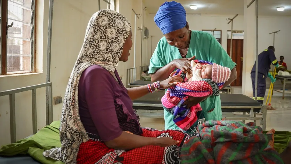 A nurse aid holds a baby while talking to the mother