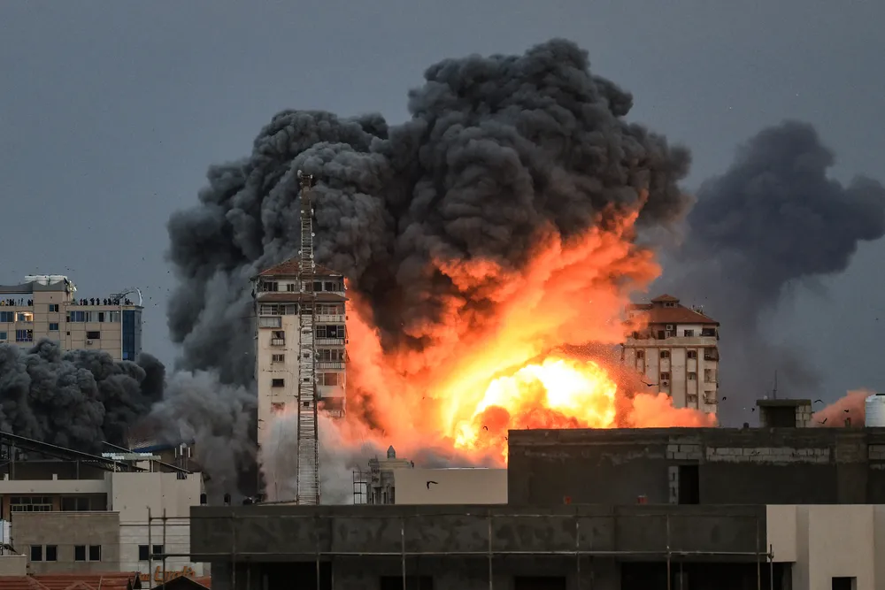 People standing on a rooftop watch as a ball of fire and smoke rises above a building in Gaza City