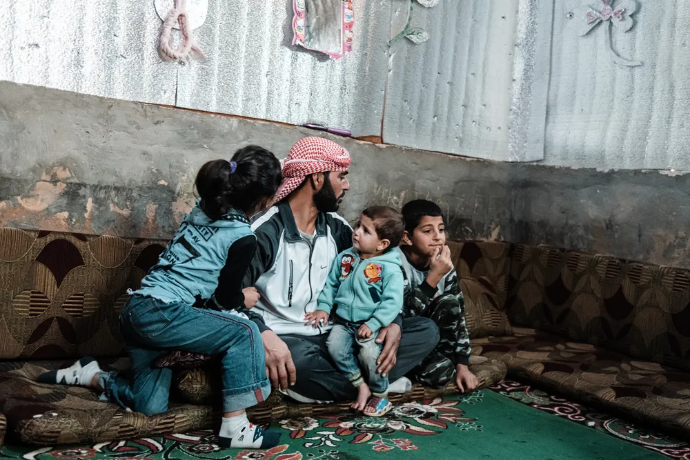 Syrian refugee Ahmed, 34, with three of his children in their makeshift shelter. His youngest daughter Zeinab, aged 18 months, was diagnosed with anaemia about four months ago. Since the economic crisis hit Lebanon the family has struggled to buy basic it