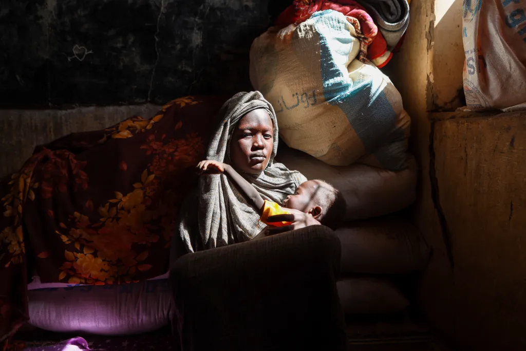 A displaced woman holds her child as she takes refuge in Alsafat Camp in Al Jazirah state.