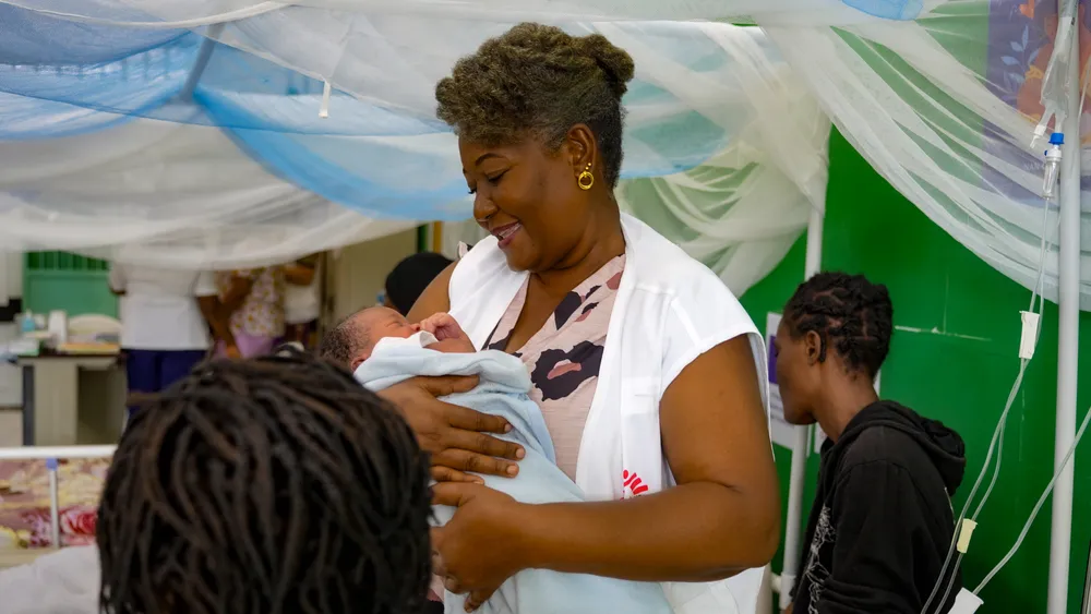 an MSF midwife at the Isaïe Jeanty maternity hospital smiles while holding a newborn in her arms